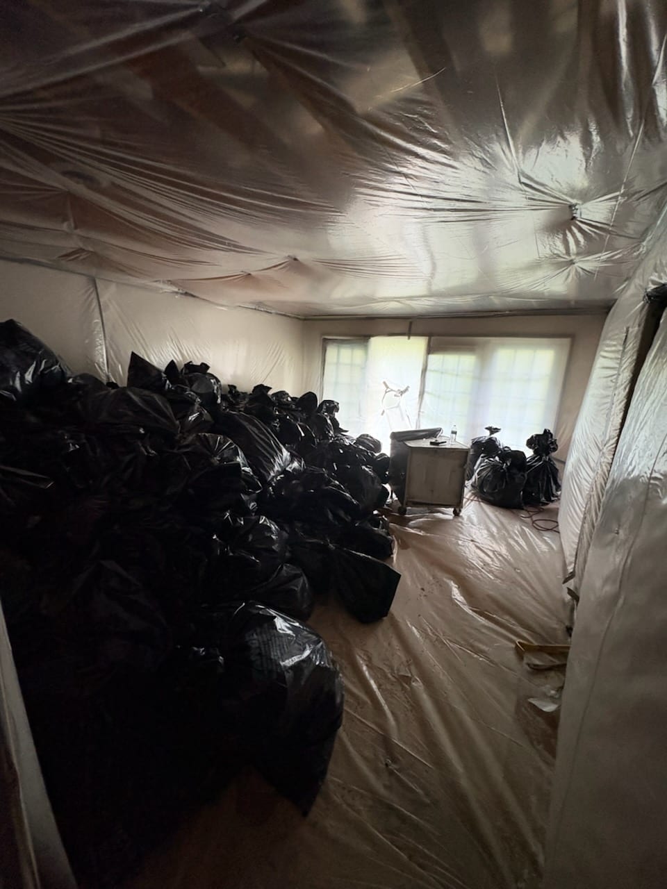 Containment set up inside a house: walls opened to the studs, plastic sheeting on floor and ceiling, and bagged debris