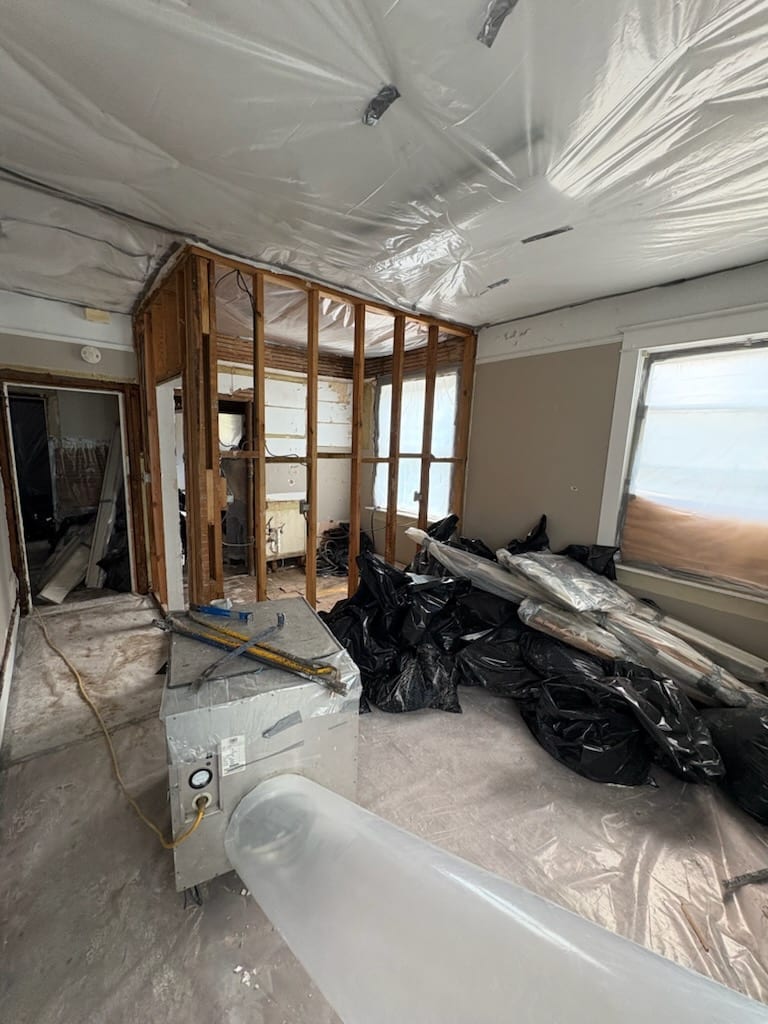 Sealed room with plastic sheeting on the ceiling and floor, piled with black bags of removed material